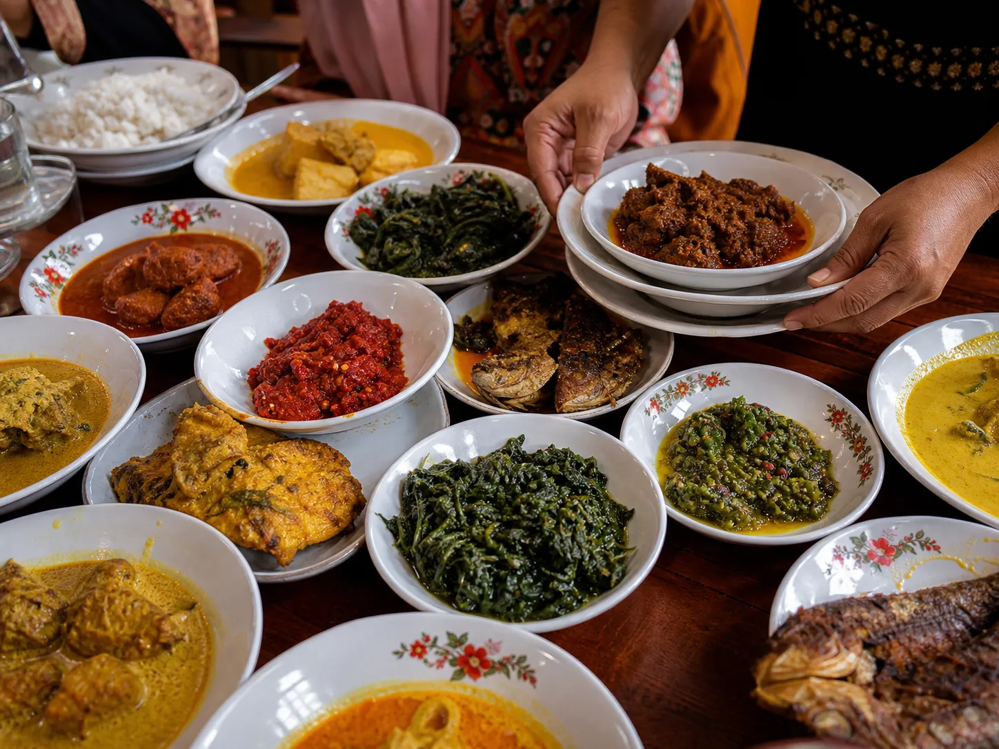 Many small plates of Padang dishes being arranged across a dining table